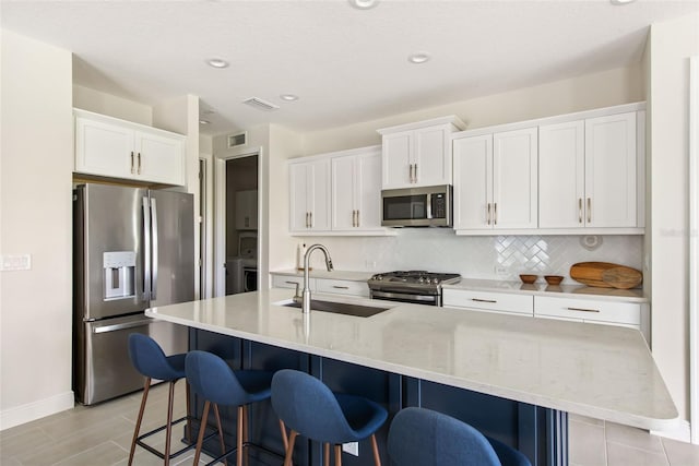 kitchen with a kitchen breakfast bar, sink, appliances with stainless steel finishes, a center island with sink, and white cabinets