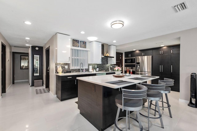 kitchen featuring backsplash, a kitchen island, sink, appliances with stainless steel finishes, and wall chimney range hood