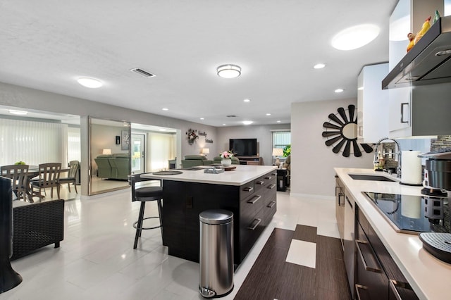 kitchen with a center island, sink, wall chimney exhaust hood, black electric cooktop, and a kitchen breakfast bar