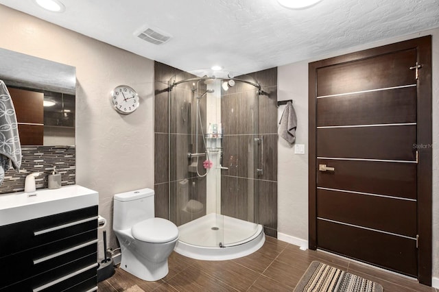 bathroom with a textured ceiling, vanity, walk in shower, tasteful backsplash, and toilet