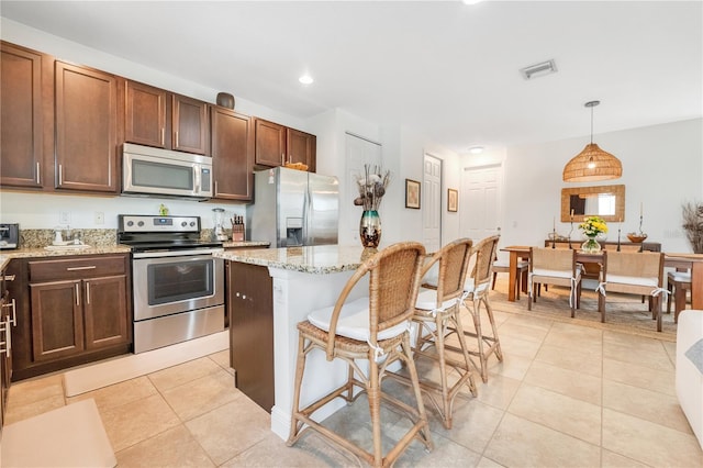 kitchen with a breakfast bar area, appliances with stainless steel finishes, light tile patterned floors, decorative light fixtures, and light stone countertops