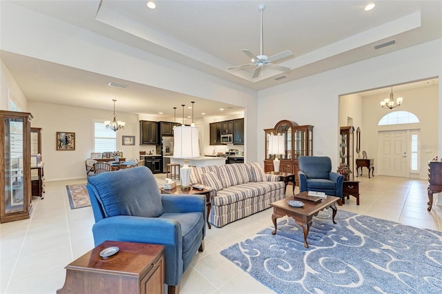 living room with ceiling fan with notable chandelier, plenty of natural light, a tray ceiling, and light tile patterned floors