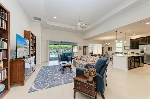 tiled living room with ceiling fan with notable chandelier, a raised ceiling, and a healthy amount of sunlight