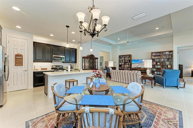 dining space with ceiling fan with notable chandelier, a textured ceiling, a tray ceiling, and light tile patterned floors