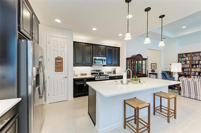 kitchen featuring decorative light fixtures, light tile patterned floors, appliances with stainless steel finishes, an island with sink, and a breakfast bar