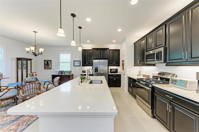 kitchen with appliances with stainless steel finishes, an island with sink, a notable chandelier, and pendant lighting