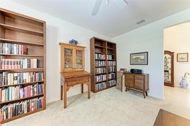 living area featuring carpet, baseboards, a textured ceiling, visible vents, and a ceiling fan