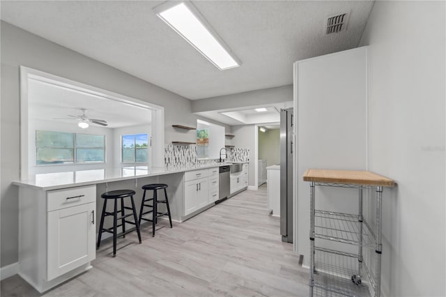 3240 Flamingo Ln, Mulberry, FL 33860 - kitchen with stainless steel appliances, white cabinets, a kitchen bar, light wood finished floors, and a textured ceiling