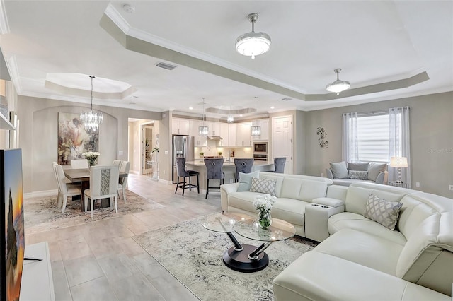 living room with crown molding, a raised ceiling, a notable chandelier, and light hardwood / wood-style flooring