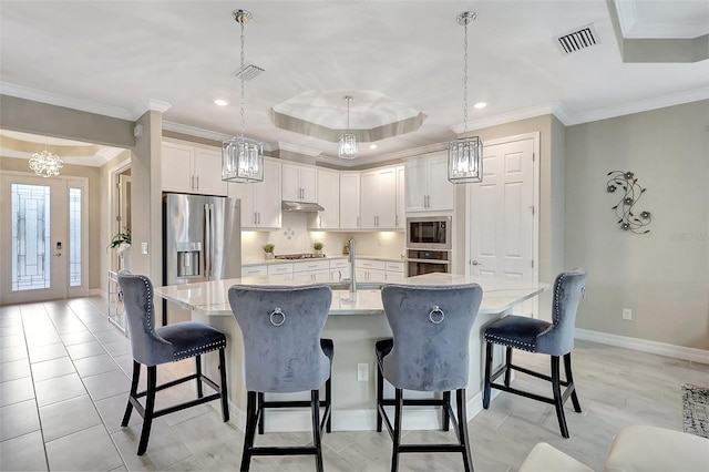 kitchen featuring decorative light fixtures, appliances with stainless steel finishes, light stone counters, a breakfast bar area, and a center island with sink