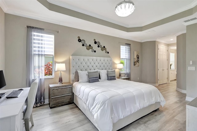 bedroom featuring multiple windows, a tray ceiling, crown molding, and light hardwood / wood-style flooring