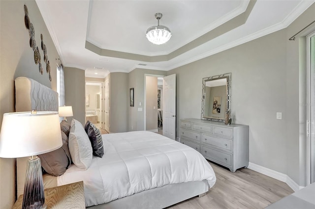 bedroom with light wood-type flooring, a tray ceiling, crown molding, and ensuite bath