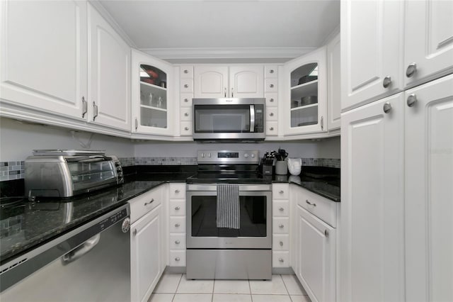 kitchen with stainless steel appliances, dark stone countertops, light tile patterned floors, and white cabinets