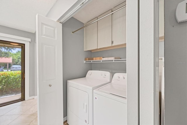 laundry area with washing machine and clothes dryer, light tile patterned flooring, and cabinets