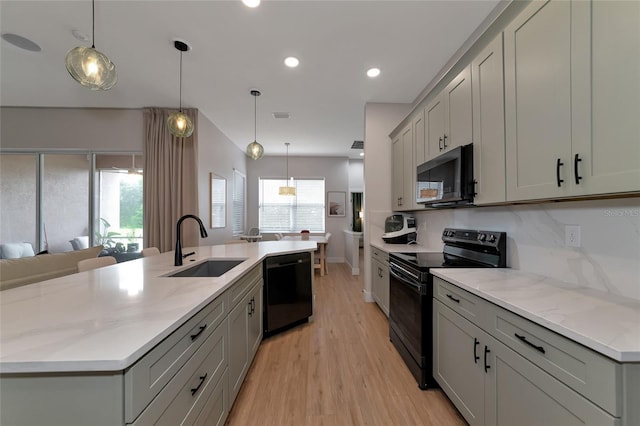 kitchen featuring light wood-type flooring, black appliances, plenty of natural light, and a kitchen island with sink