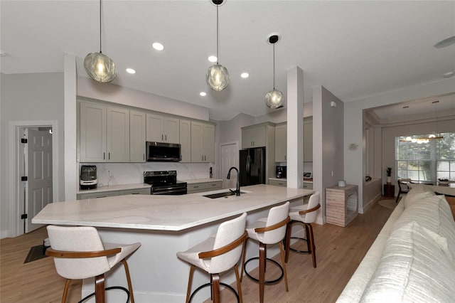 kitchen with light wood-type flooring, black appliances, sink, and a kitchen breakfast bar