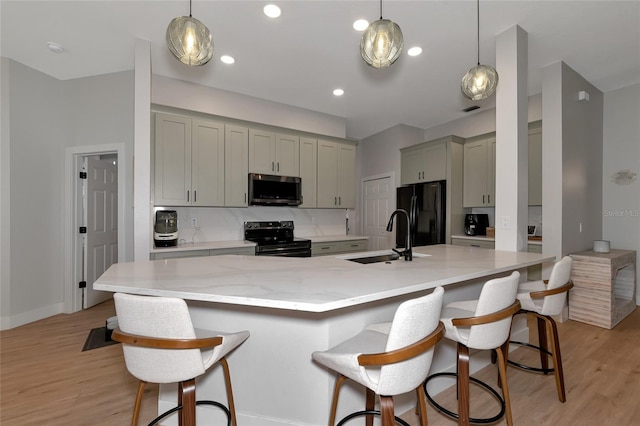 kitchen featuring black appliances, a breakfast bar, sink, gray cabinets, and light wood-type flooring