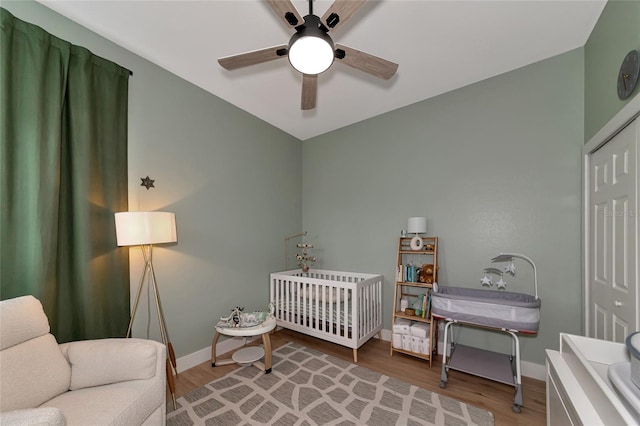 bedroom with a closet, wood-type flooring, a nursery area, and ceiling fan