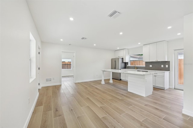 kitchen with white cabinetry, sink, stainless steel fridge, a kitchen island, and light wood-type flooring