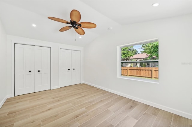 unfurnished bedroom featuring light wood-type flooring, two closets, ceiling fan, and lofted ceiling