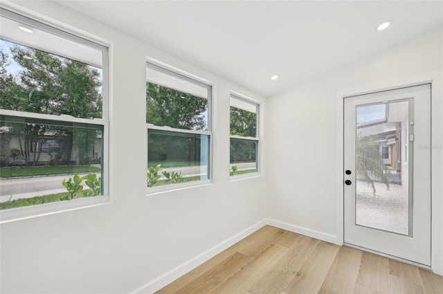 doorway to outside with light wood-type flooring, plenty of natural light, and lofted ceiling