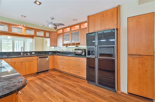 kitchen with a sink, light wood-style floors, stainless steel dishwasher, black fridge, and glass insert cabinets