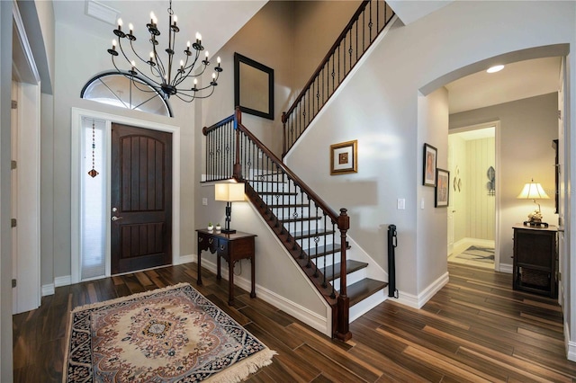 entryway featuring a towering ceiling, dark wood-type flooring, and a notable chandelier