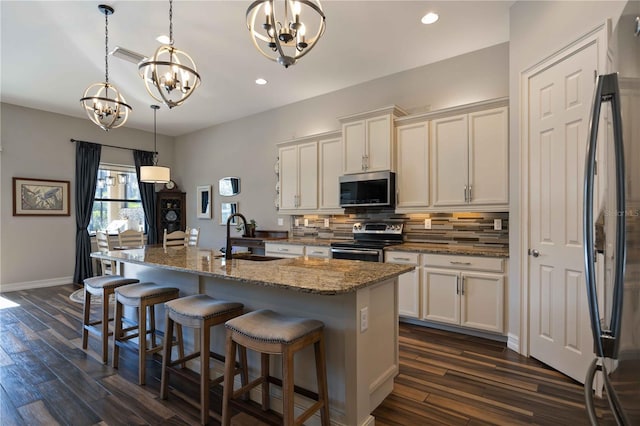 kitchen featuring appliances with stainless steel finishes, a chandelier, sink, dark wood-type flooring, and a kitchen island with sink