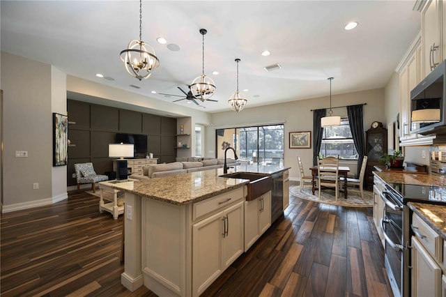 kitchen with light stone countertops, decorative light fixtures, a kitchen island with sink, dark wood-type flooring, and stainless steel appliances