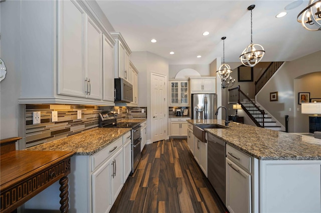 kitchen featuring white cabinetry, decorative light fixtures, stainless steel appliances, dark hardwood / wood-style floors, and a center island with sink