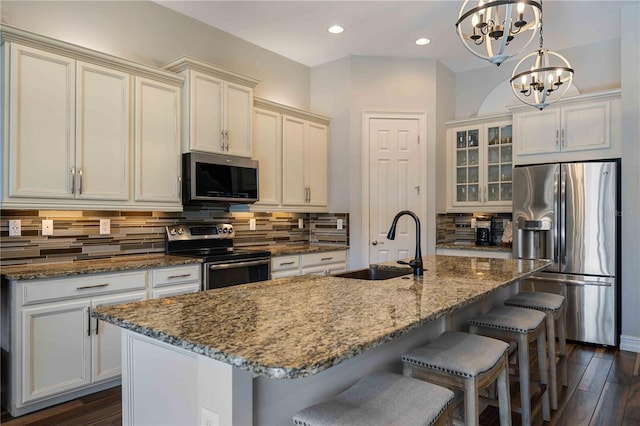 kitchen featuring a notable chandelier, an island with sink, hanging light fixtures, dark hardwood / wood-style floors, and appliances with stainless steel finishes