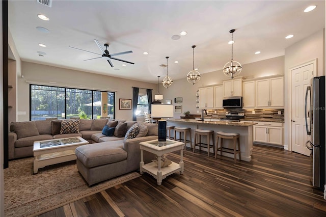 living room with ceiling fan with notable chandelier, dark wood-type flooring, and sink