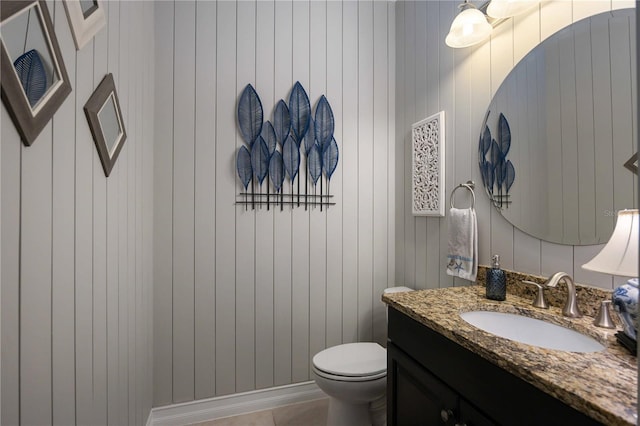 bathroom featuring vanity, toilet, and wooden walls