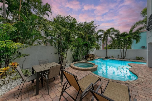 pool at dusk featuring a patio area and an in ground hot tub