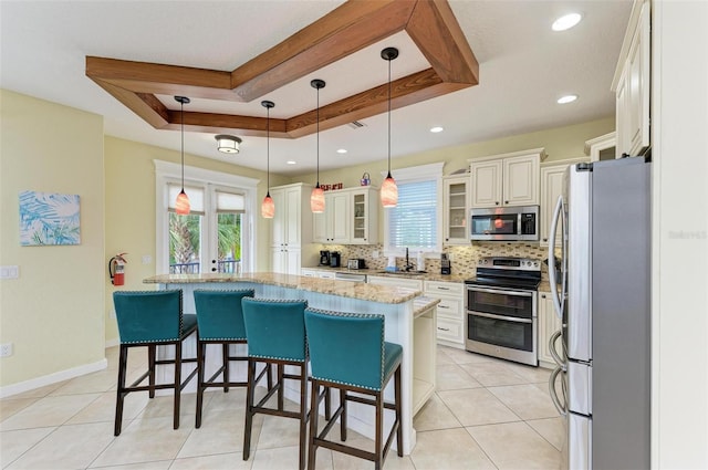 kitchen with plenty of natural light, stainless steel appliances, a raised ceiling, and hanging light fixtures