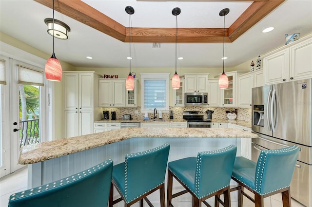 kitchen with pendant lighting, a kitchen island, stainless steel appliances, and a raised ceiling