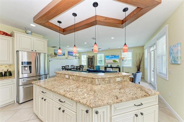 kitchen featuring light stone counters, a center island, hanging light fixtures, stainless steel refrigerator with ice dispenser, and a raised ceiling