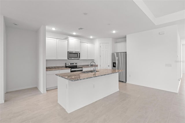 kitchen featuring sink, dark stone counters, a kitchen island with sink, white cabinets, and appliances with stainless steel finishes