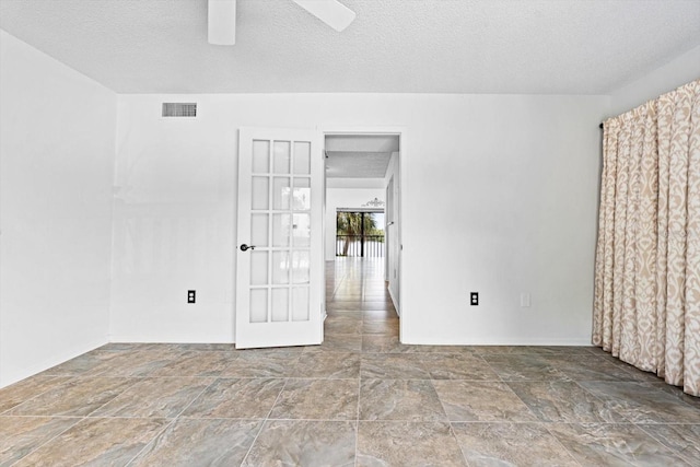 empty room featuring a ceiling fan, baseboards, visible vents, and a textured ceiling