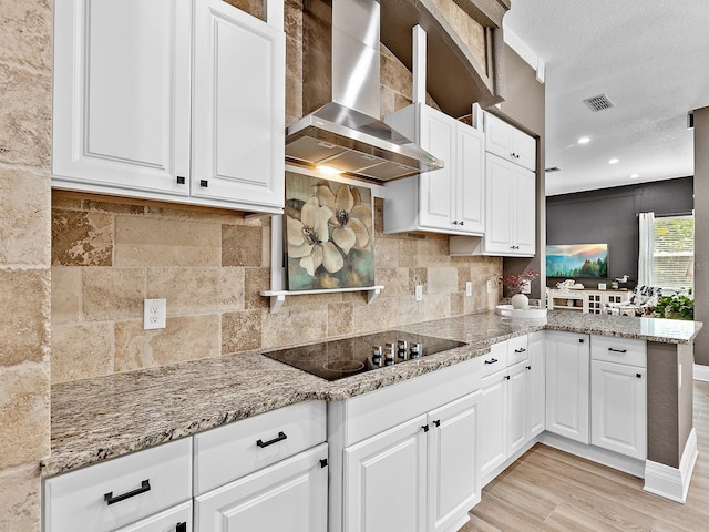 kitchen with black electric stovetop, wall chimney exhaust hood, white cabinetry, and light hardwood / wood-style floors