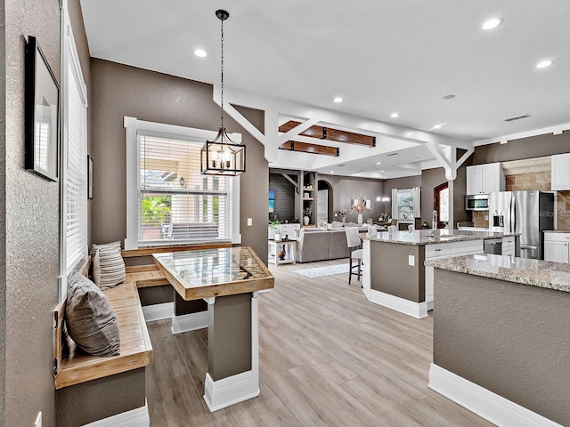 kitchen with appliances with stainless steel finishes, light hardwood / wood-style floors, a center island, light stone counters, and white cabinets