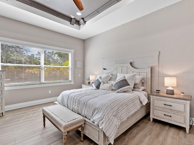 bedroom with a tray ceiling, a textured ceiling, light hardwood / wood-style flooring, and ceiling fan