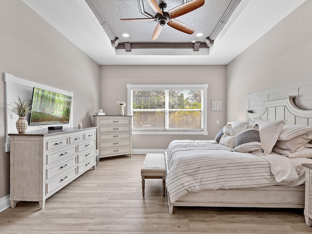 bedroom with a tray ceiling, a textured ceiling, light hardwood / wood-style flooring, and ceiling fan