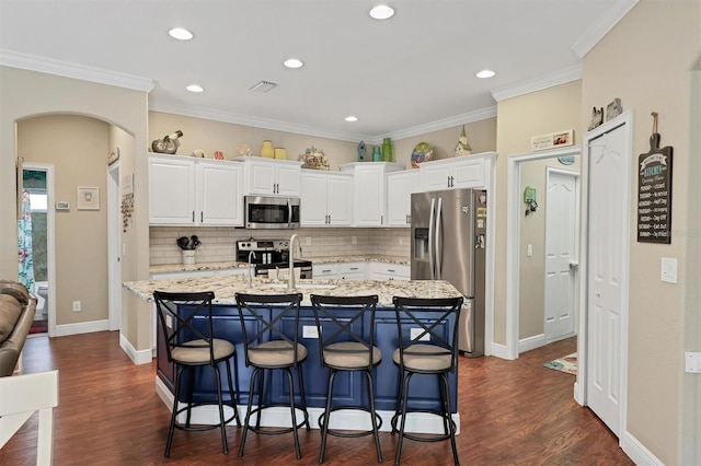 kitchen with an island with sink, a breakfast bar area, appliances with stainless steel finishes, and dark hardwood / wood-style flooring