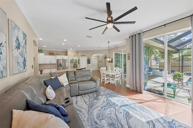 living room with ceiling fan with notable chandelier, light wood-type flooring, and crown molding