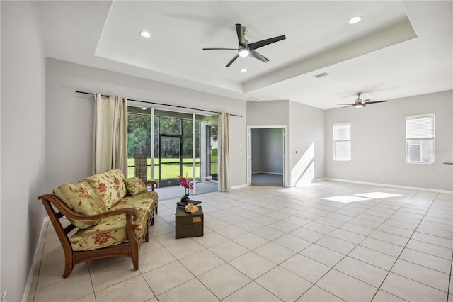 tiled living room with a raised ceiling and ceiling fan