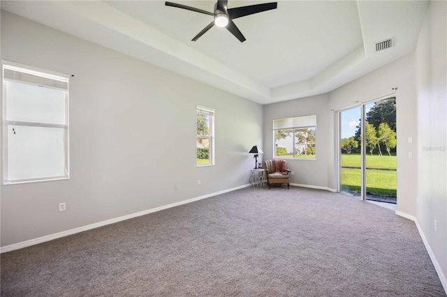 unfurnished room with ceiling fan, a raised ceiling, a healthy amount of sunlight, and carpet flooring