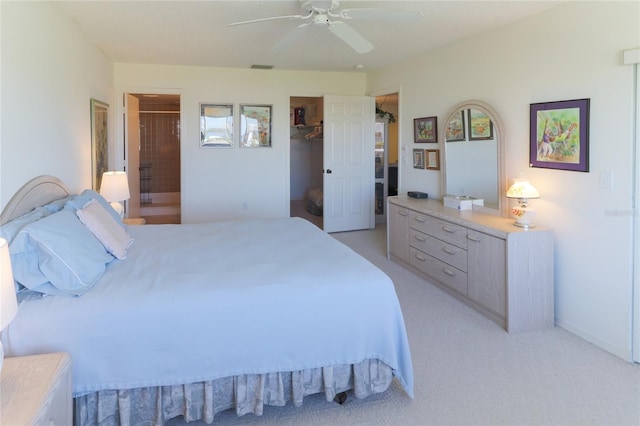 bedroom with light carpet, visible vents, a ceiling fan, a walk in closet, and ensuite bath