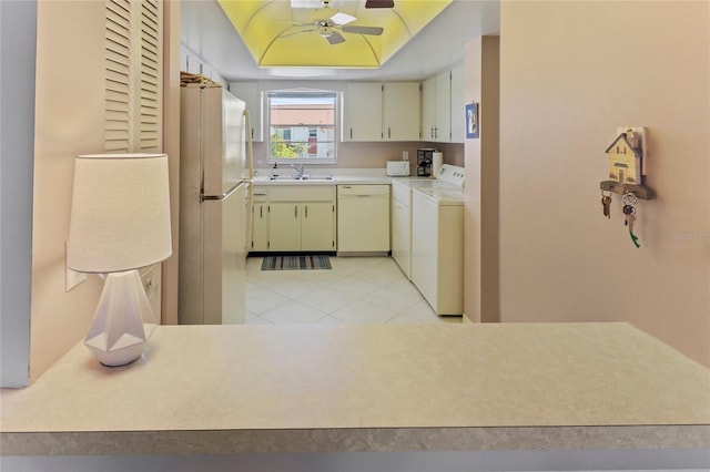 kitchen with a tray ceiling, light countertops, a sink, washer and dryer, and white appliances