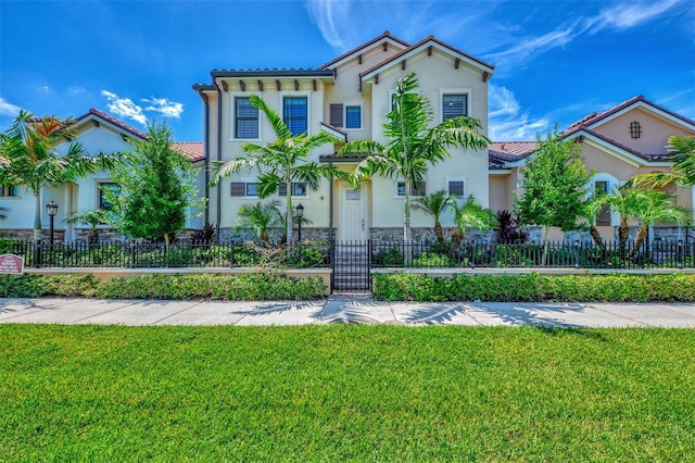 mediterranean / spanish home featuring stucco siding, stone siding, a fenced front yard, a front yard, and a tile roof